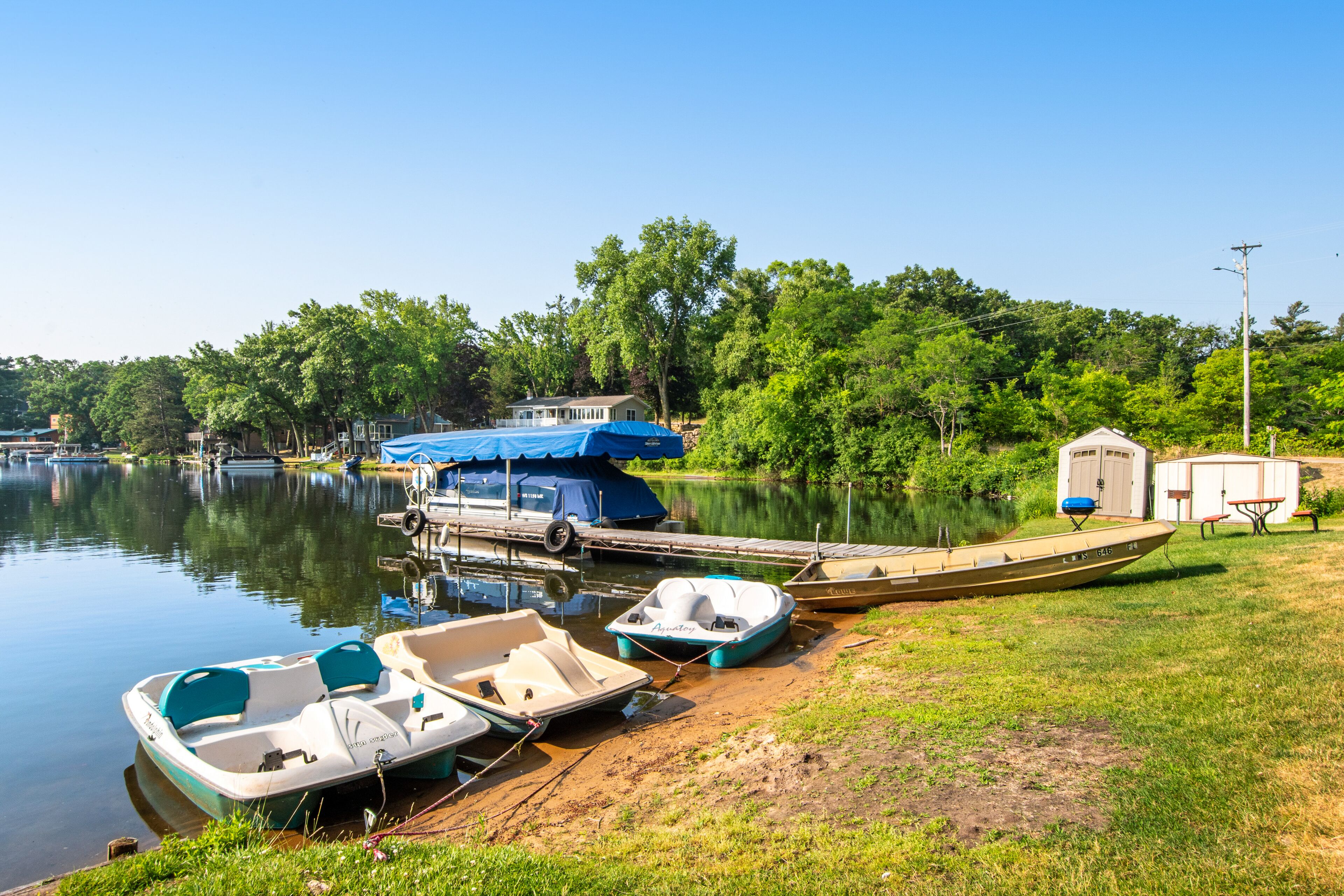 A lakeside dock with several boats, a covered area, and a small building.