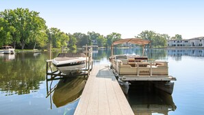 A dock with two boats, one with a canopy and another without, on a calm lake with trees and buildings in the background. - Thunderbird Resort Condo (Wisconsin Dells)