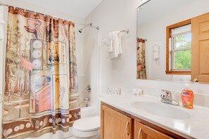 A bathroom with a shower curtain, toilet, sink, and wooden cabinets. - Thunderbird Resort Condo (Wisconsin Dells)