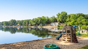A lakeside park with a playground, including a slide and climbing structure, near a calm lake. - Thunderbird Resort Condo (Wisconsin Dells)