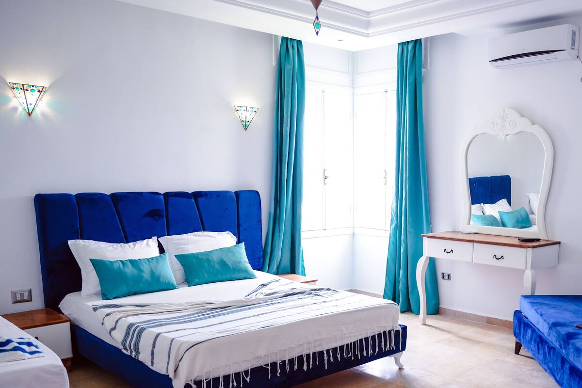 Een slaapkamer met een groot bed, een nachtkastje, een dressoir en een spiegel.
