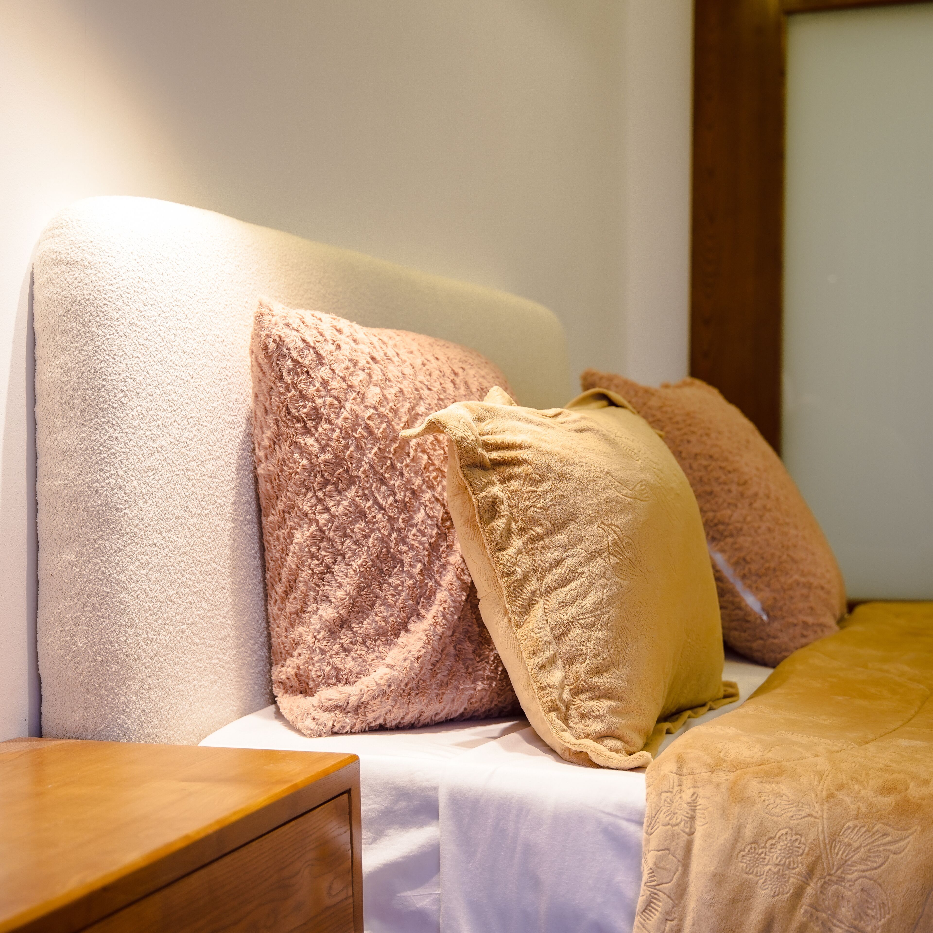 A bed with a white mattress and two pillows, one pink and one beige.