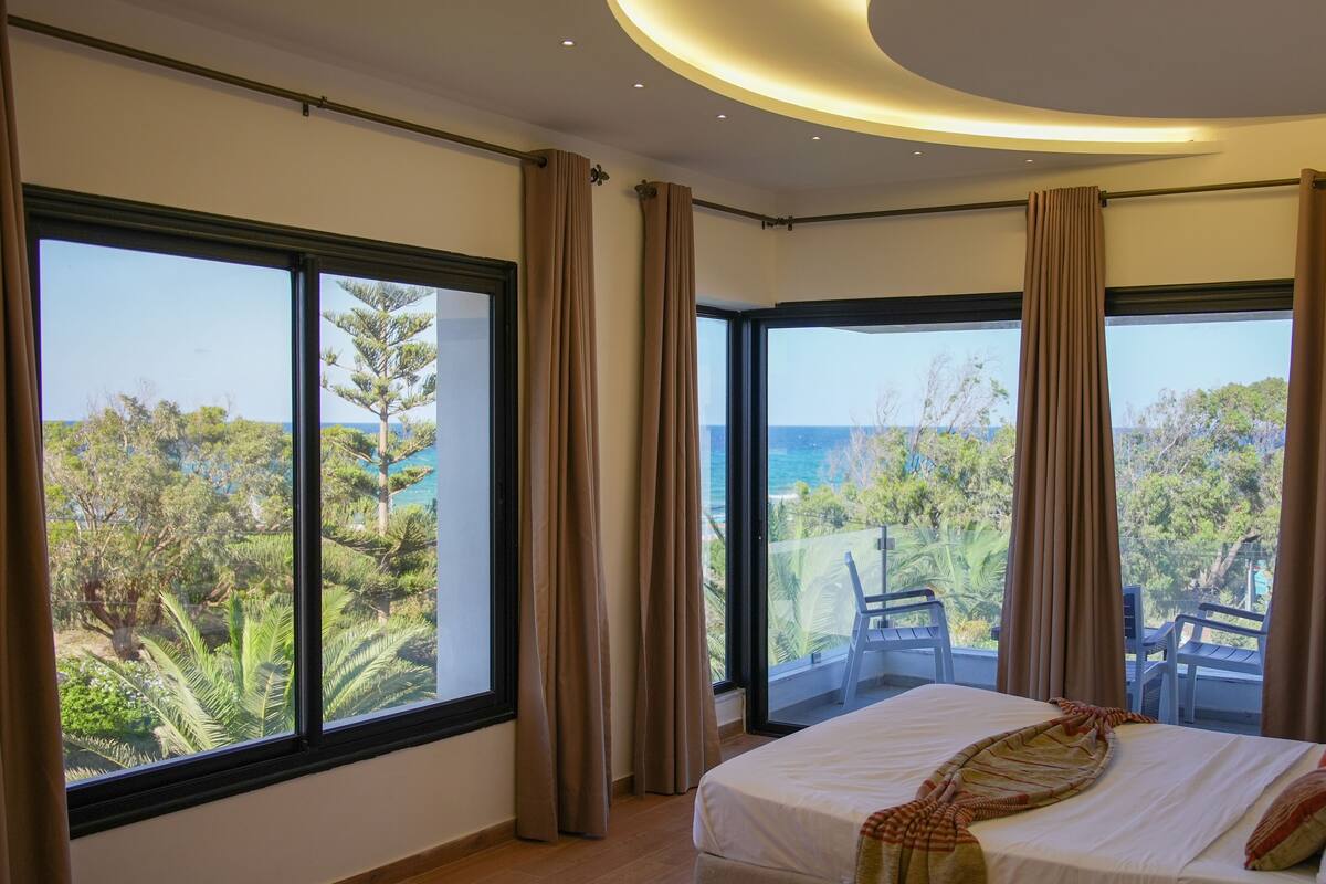 Een slaapkamer met een groot bed, uitzicht op de oceaan en een balkon met een stoel.