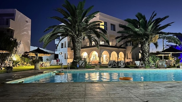 A swimming pool with palm trees, a building with arched windows, and outdoor seating. -  Dar Oguz (Hammam Al Agzaz)
