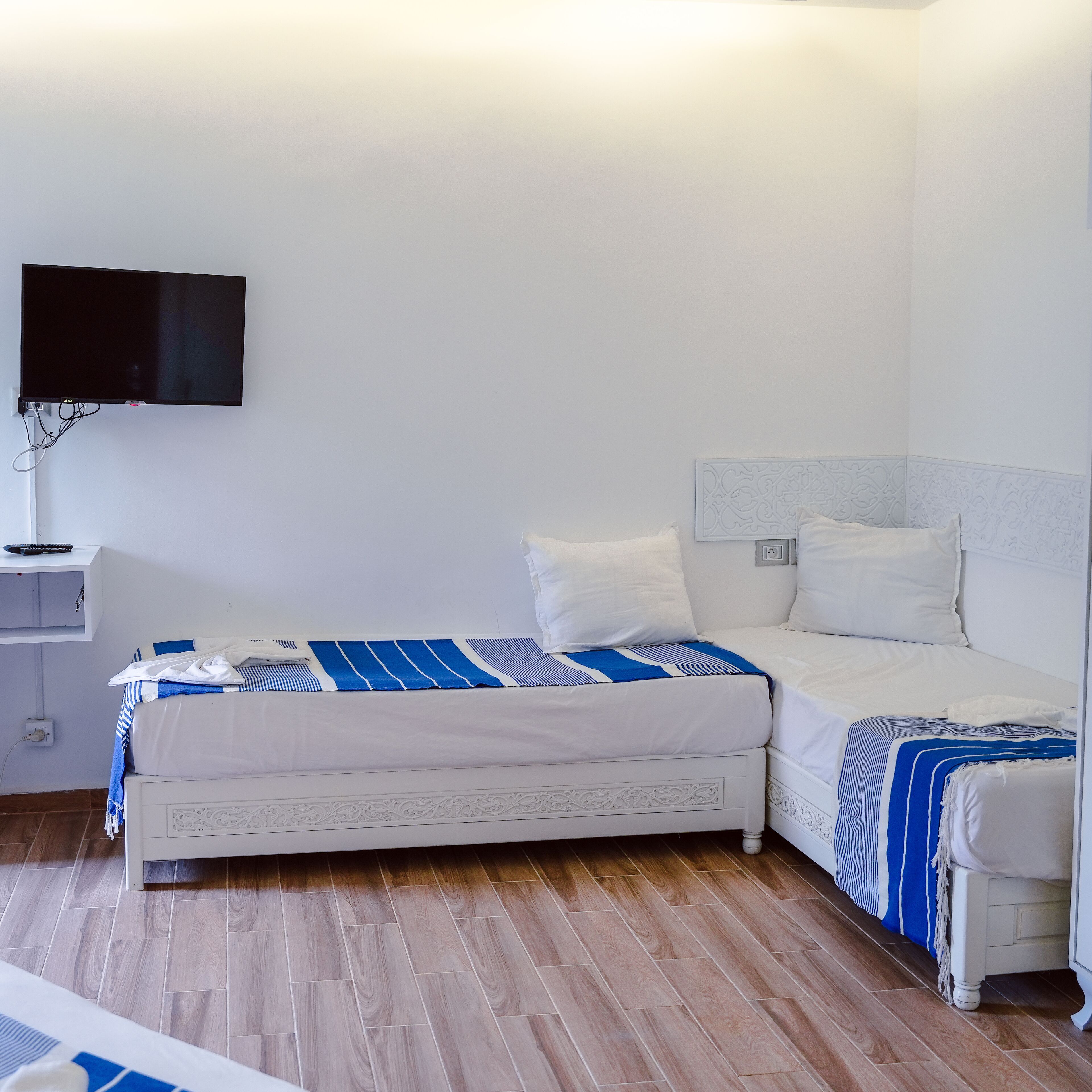 A bedroom with two beds, a TV mounted on the wall, and a bedside table.