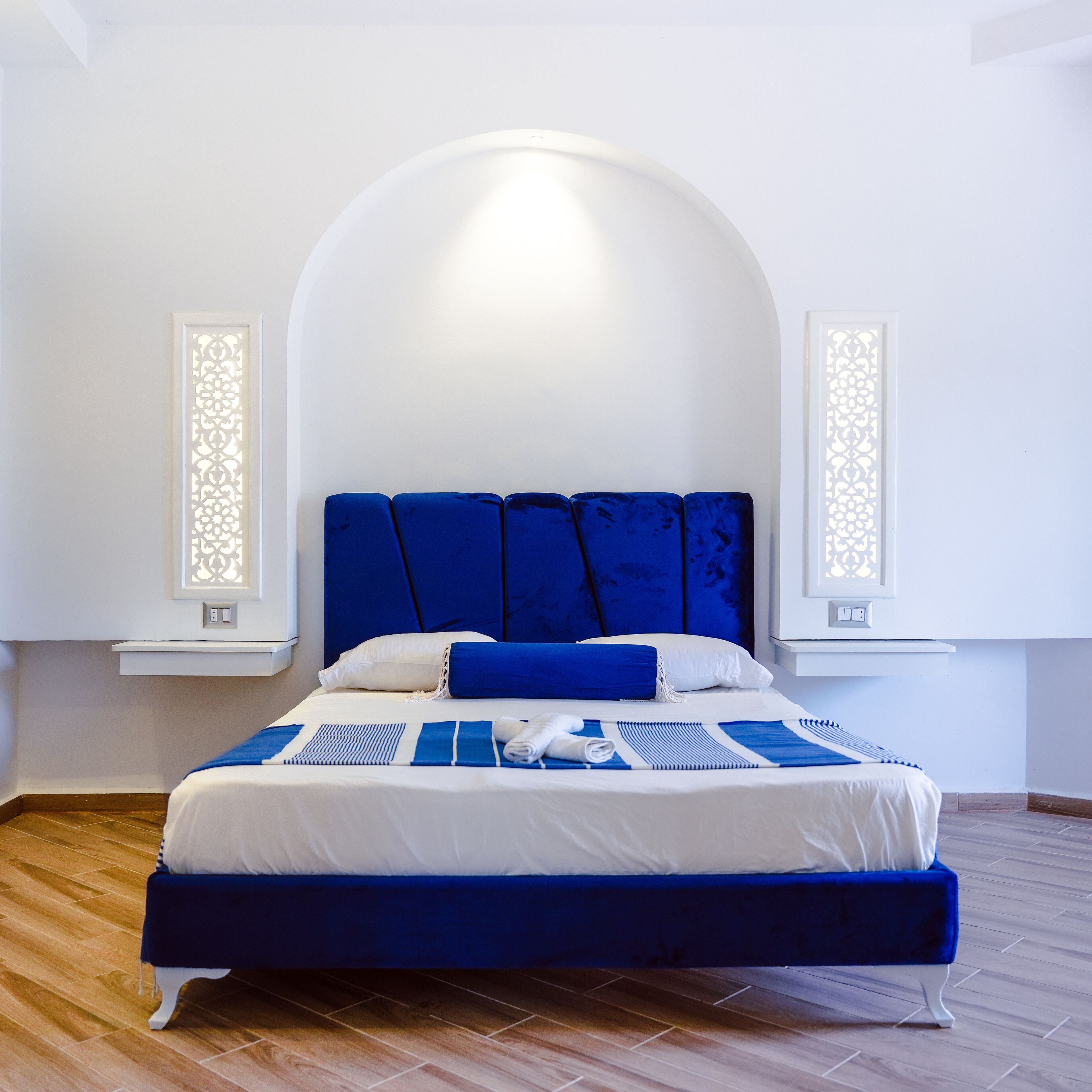 A modern bedroom with a large bed, white walls, and a wooden floor.