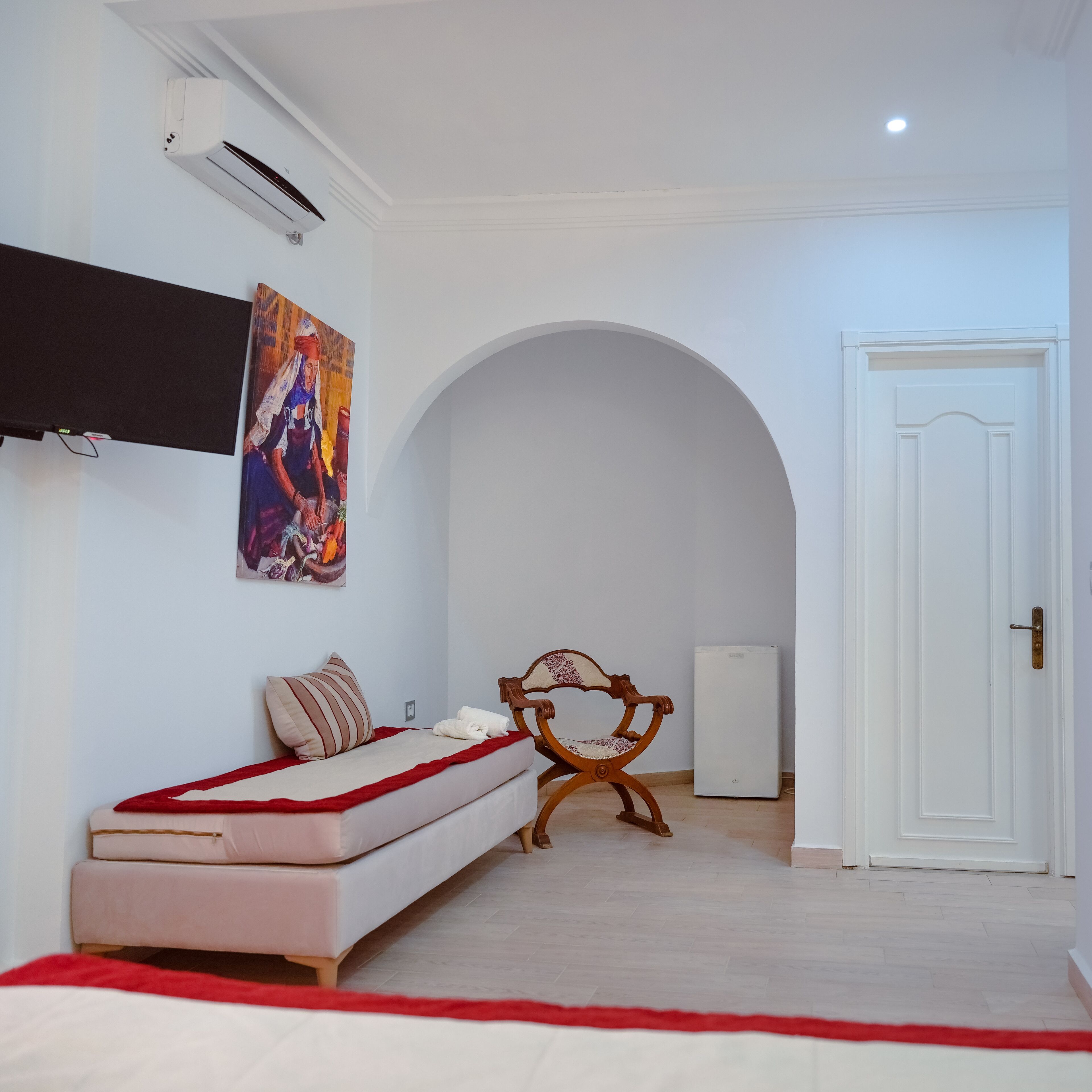 A bedroom with a bed, a chair, a painting, an air conditioning unit, and a door.