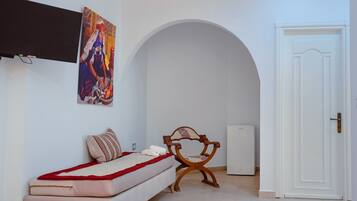 A bedroom with a bed, a chair, a painting, an air conditioning unit, and a door.