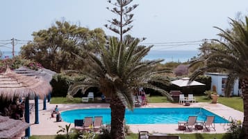Relax by the serene pool surrounded by lush greenery and palm trees, with lounge chairs and umbrellas providing shade.