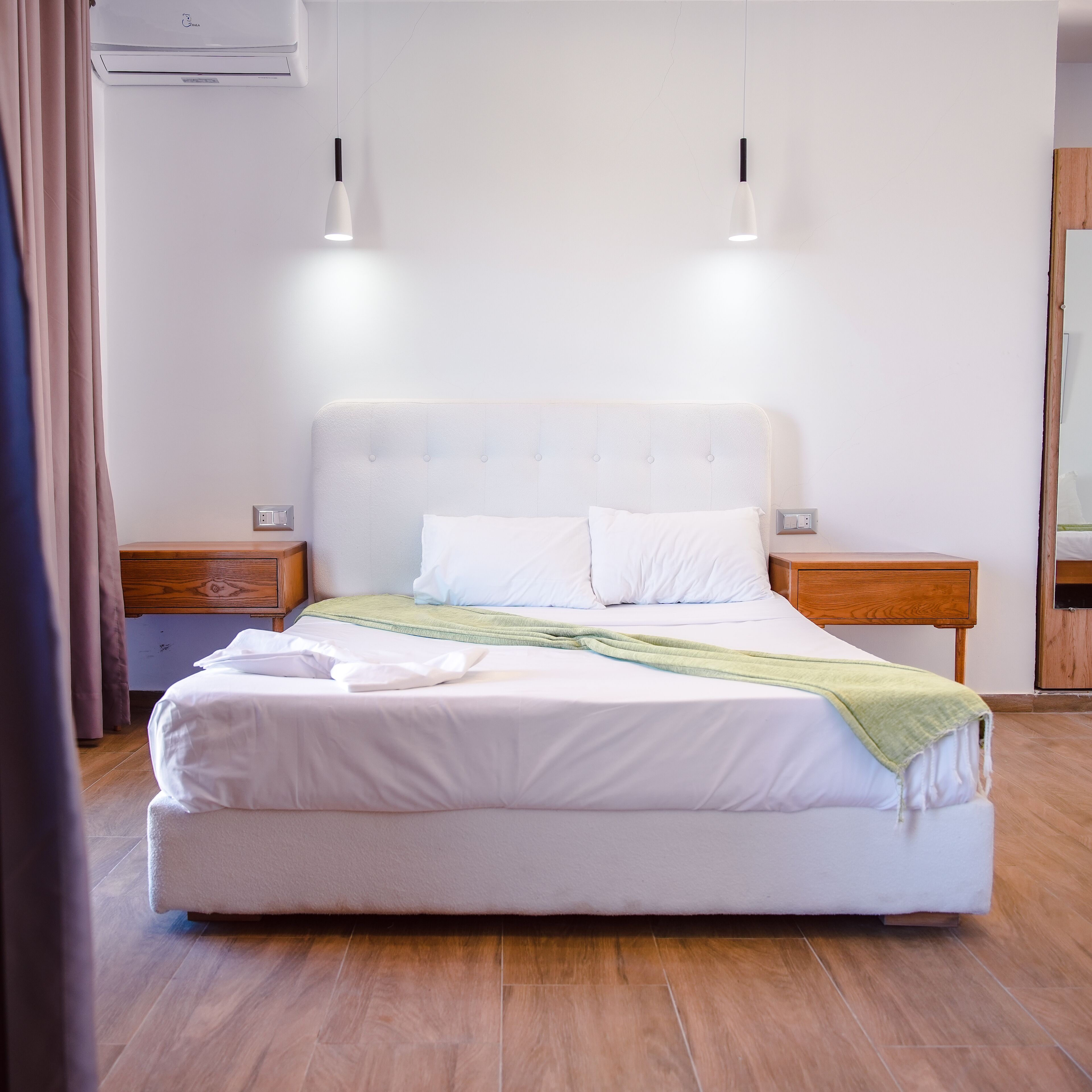 Una cama bien tendida con sábanas blancas, dos mesitas de noche con lámparas y un cabecero de madera.