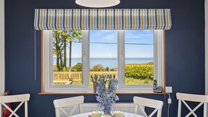 Un comedor con una mesa, sillas, un ventanal con vista al mar y una lámpara colgante.
