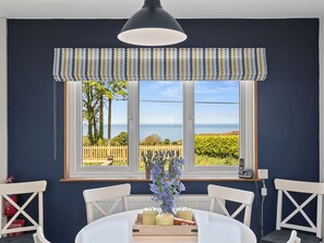 Un comedor con una mesa, sillas, un ventanal con vista al mar y una lámpara colgante.