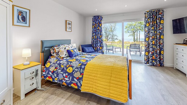 Un dormitorio con cama, mesita de noche, lámpara y vistas al exterior.