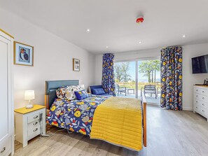 Un dormitorio con cama, mesita de noche, lámpara y vistas al exterior.