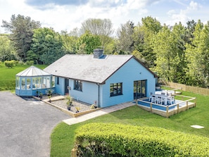 Una casa azul con un invernadero, piscina y un jardín bien cuidado.
