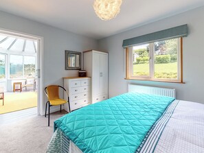 Un dormitorio con cama, armario, silla, ventana con vistas y puerta que da a un balcón.