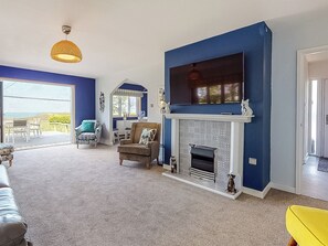 Una sala de estar con chimenea, un televisor montado encima y vistas a un balcón a través de una puerta abierta.