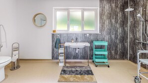 Un baño moderno con un lavamanos blanco, un espejo, una ventana, una ducha y un carro de almacenamiento color turquesa.