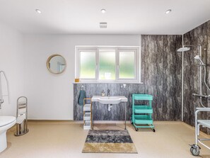 Un baño moderno con un lavamanos blanco, un espejo, una ventana, una ducha y un carro de almacenamiento color turquesa.