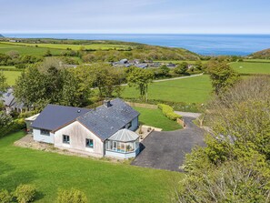 Una casa costera con un amplio jardín, un invernadero y vista al mar.