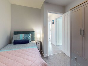 Un dormitorio con cama, mesita de noche, lámpara, armario y una puerta abierta que da a otra habitación.