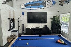 A pool table with a single white cue ball, a television mounted on the wall, and a surfboard decoration.