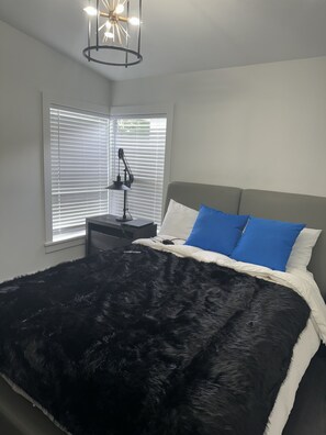 A bedroom with a bed, a nightstand, a lamp, and a window with blinds.