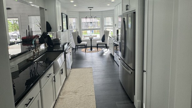 A modern kitchen with white cabinets, a black countertop, and a large refrigerator. There is a dining area with two chairs and a table in the center.