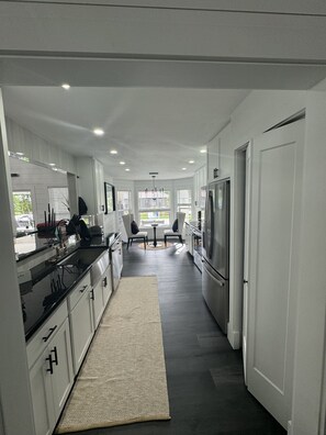 A modern kitchen with white cabinets, a black countertop, and a large refrigerator. There is a dining area with two chairs and a table in the center. - JUST IN TIME FOR SEASON! (Bonita Springs)