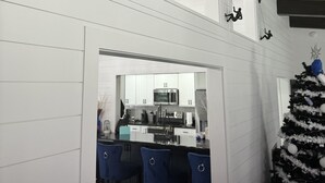 A modern kitchen with white cabinetry and a central island, a dining area with blue chairs, and a decorated Christmas tree.