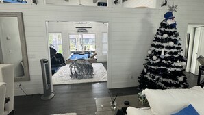 A modern living room with a large Christmas tree, a white sofa, and a view into the dining area.