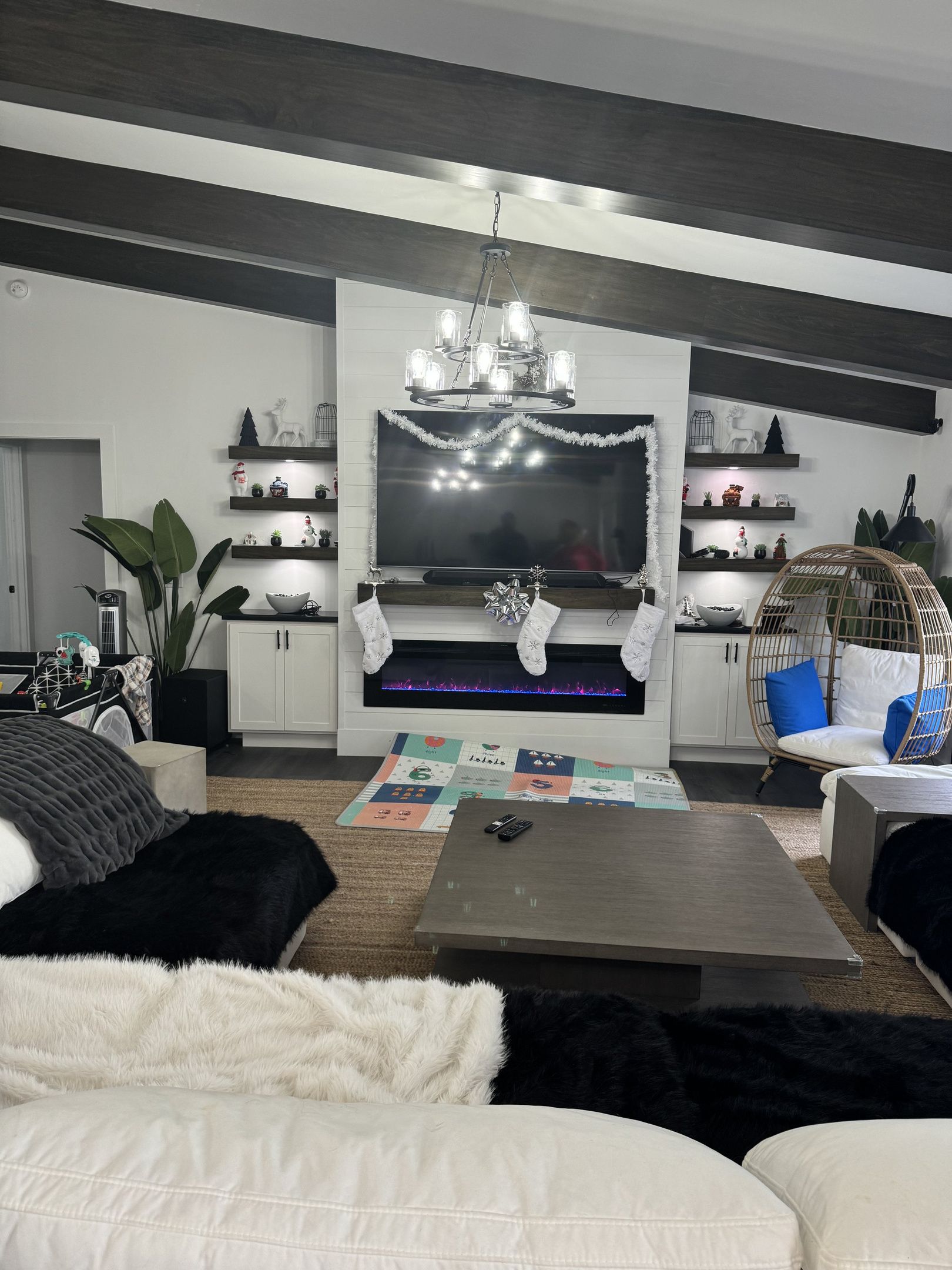 A modern living room with a fireplace, a chandelier, and a large flat-screen TV.