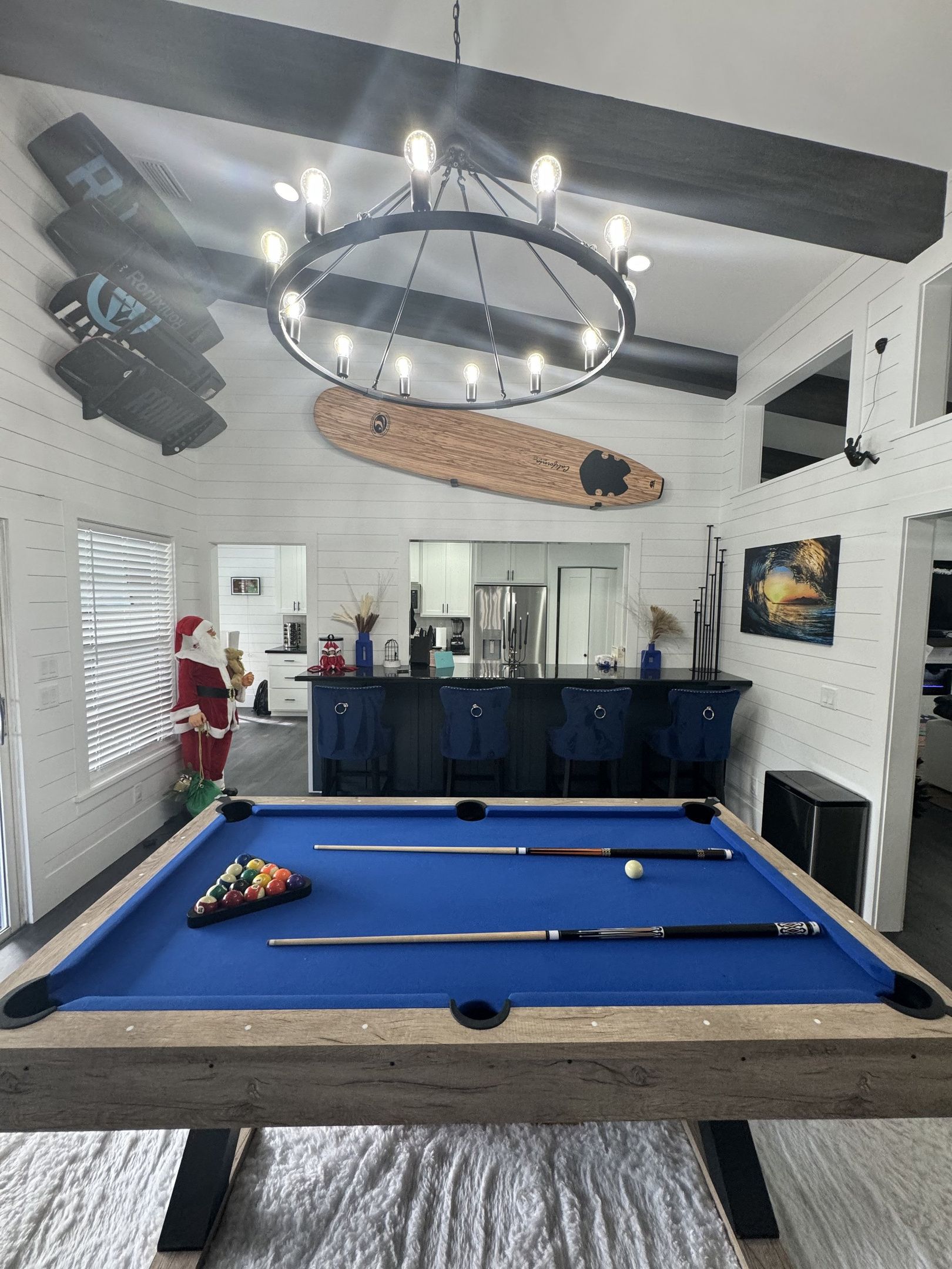 A pool table with a wooden frame, a bar area with stools, and a ceiling light fixture.