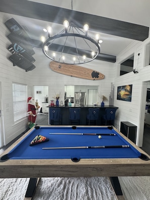 A pool table with a wooden frame, a bar area with stools, and a ceiling light fixture. - The Board Room - A Unique Experience (Bonita Springs)