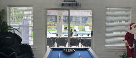 A pool table in a room with a chandelier, skateboards on the wall, and a view of the outside.