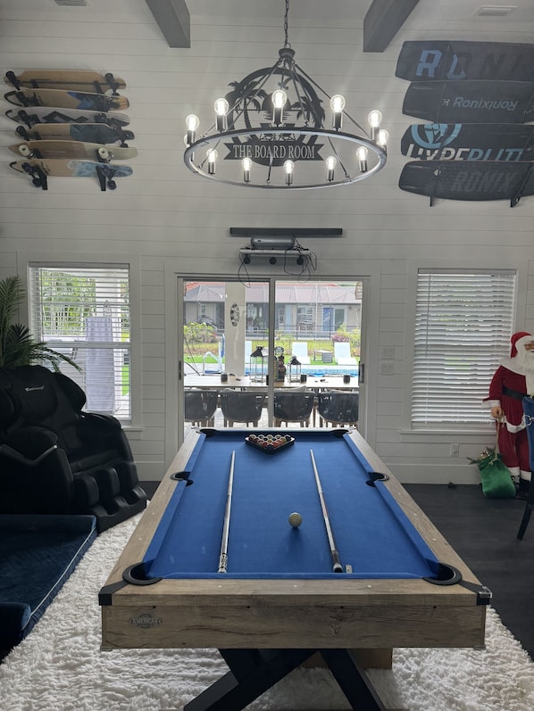 A pool table in a room with a chandelier, skateboards on the wall, and a view of the outside. - The Board Room - A Unique Experience (Bonita Springs)