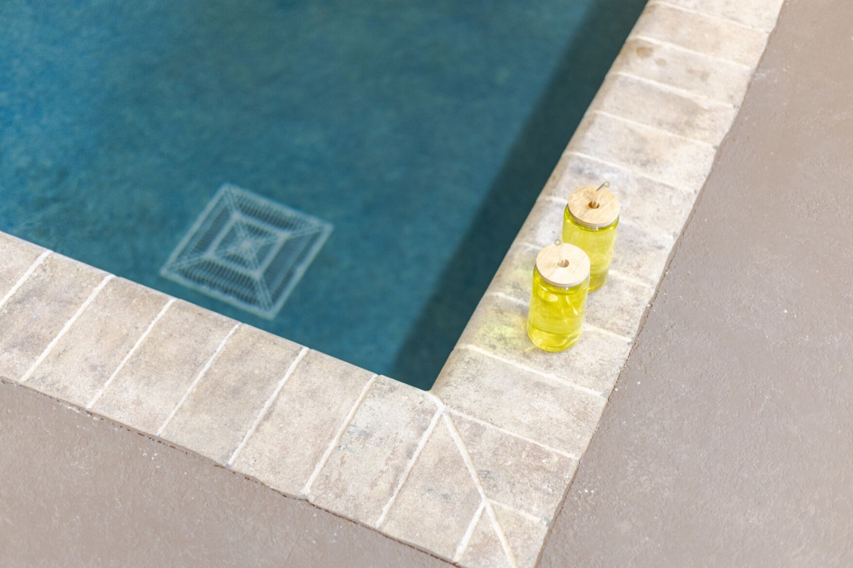 Una piscina con bordo piastrellato e due bottiglie gialle ai lati.