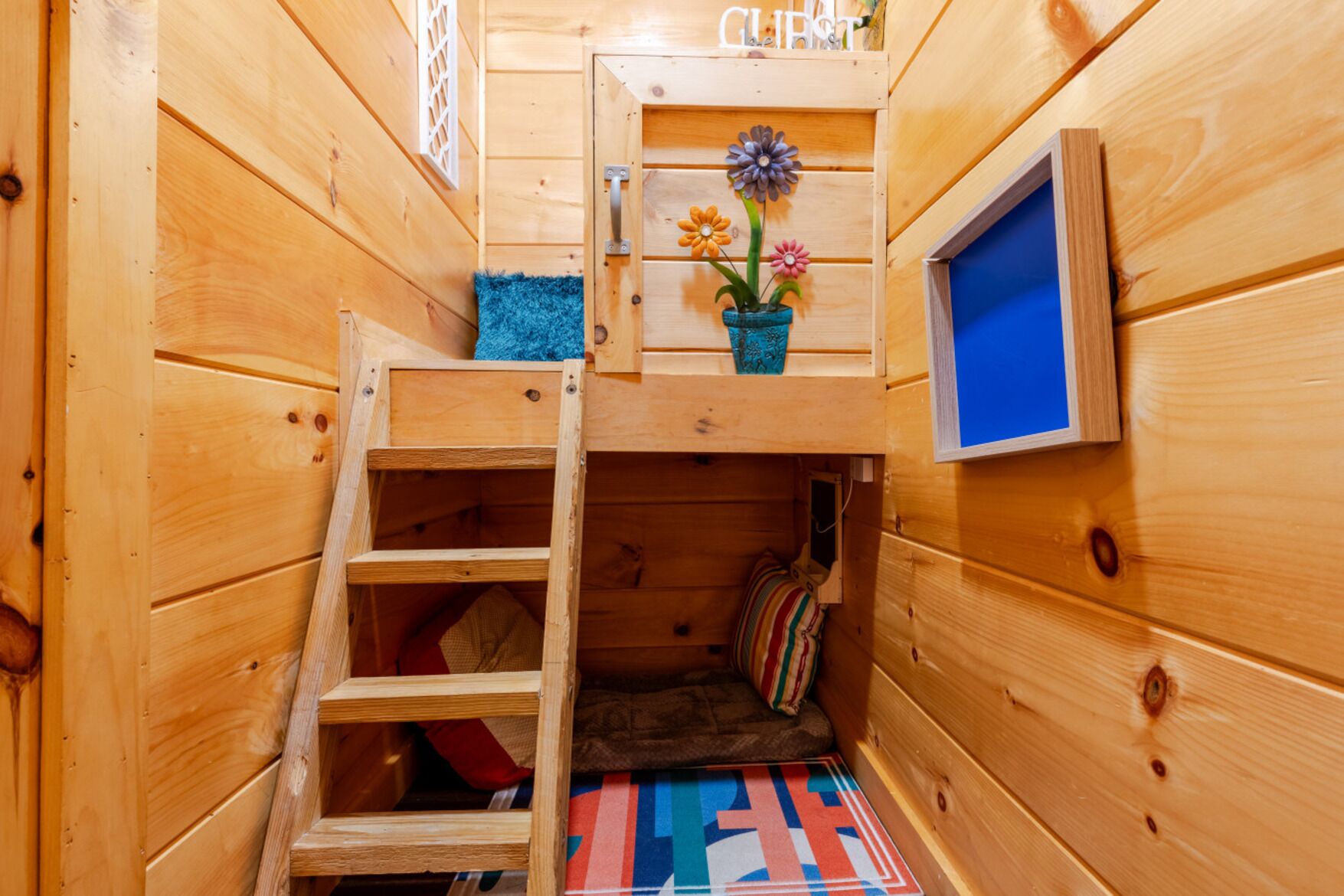 Eine Holzhütte mit Schlafkoje, einem kleinen Fenster und einer blauen Matte auf dem Boden.