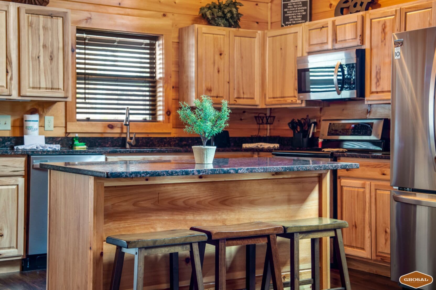 Une cuisine avec des meubles en bois, un plan de travail en granit, un réfrigérateur en acier inoxydable et une plante en pot.