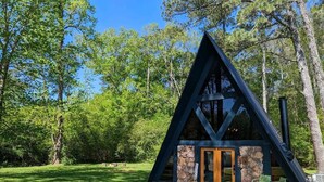 A cabin with a stone foundation and dark wooden beams, surrounded by lush greenery. - Cozy A-Frame Cabin | Lake Access + Fire Pit (Guntersville)