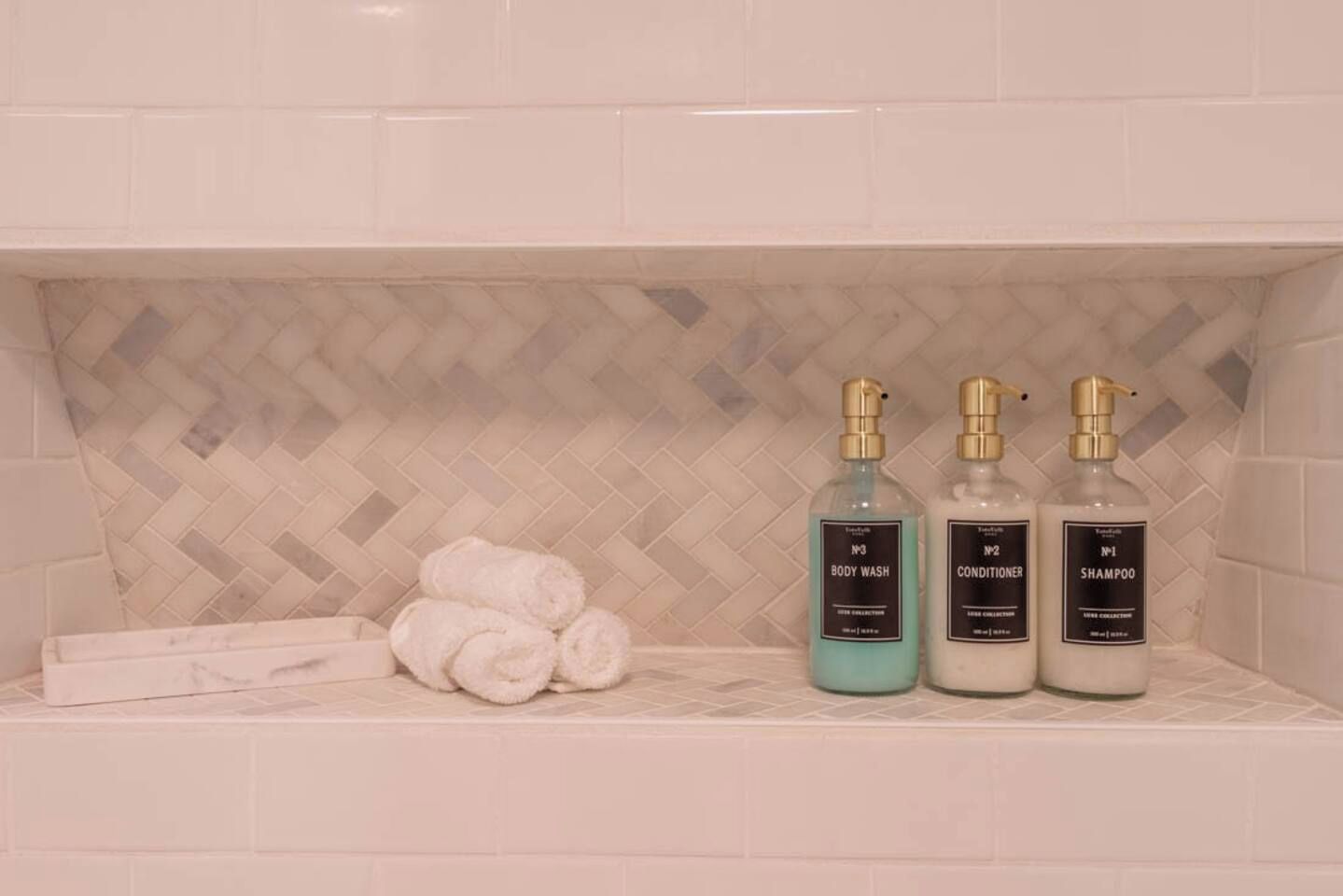 A bathroom shelf with three bottles of toiletries and a stack of white towels.