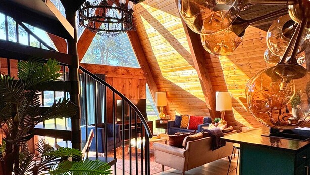 A spacious loft with a high ceiling, a spiral staircase, and a cozy seating area with a fireplace. - Cozy A-Frame Cabin | Lake Access + Fire Pit (Guntersville)