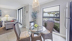 Un salon moderne avec une table à manger au plateau en verre, des chaises en osier, un canapé, une lampe et une vue sur l’océan grâce à de grandes fenêtres.