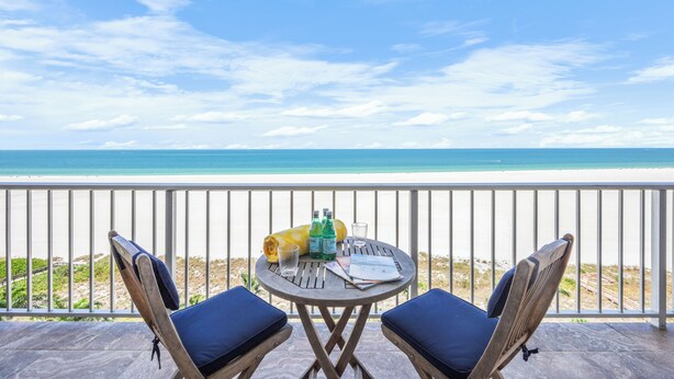 A balcony with two chairs and a table, overlooking a beach. - Breezy Beachfront Condo | Panoramic Beach View (Marco Island)