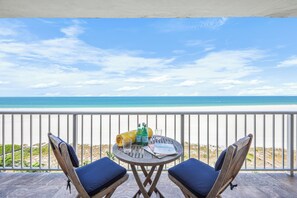 Balcón con dos sillas y una mesa, con vista a la playa.