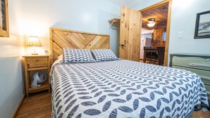 Un dormitorio con cabecera de madera, cama con ropa de cama estampada, mesita de noche con lámpara y armario de madera.