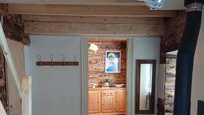 A rustic interior with a wooden staircase, a black wood stove, and a kitchen visible through an open door. - The “Cabane des Deux Soeurs”  (Le Bourg-d'Oisans)