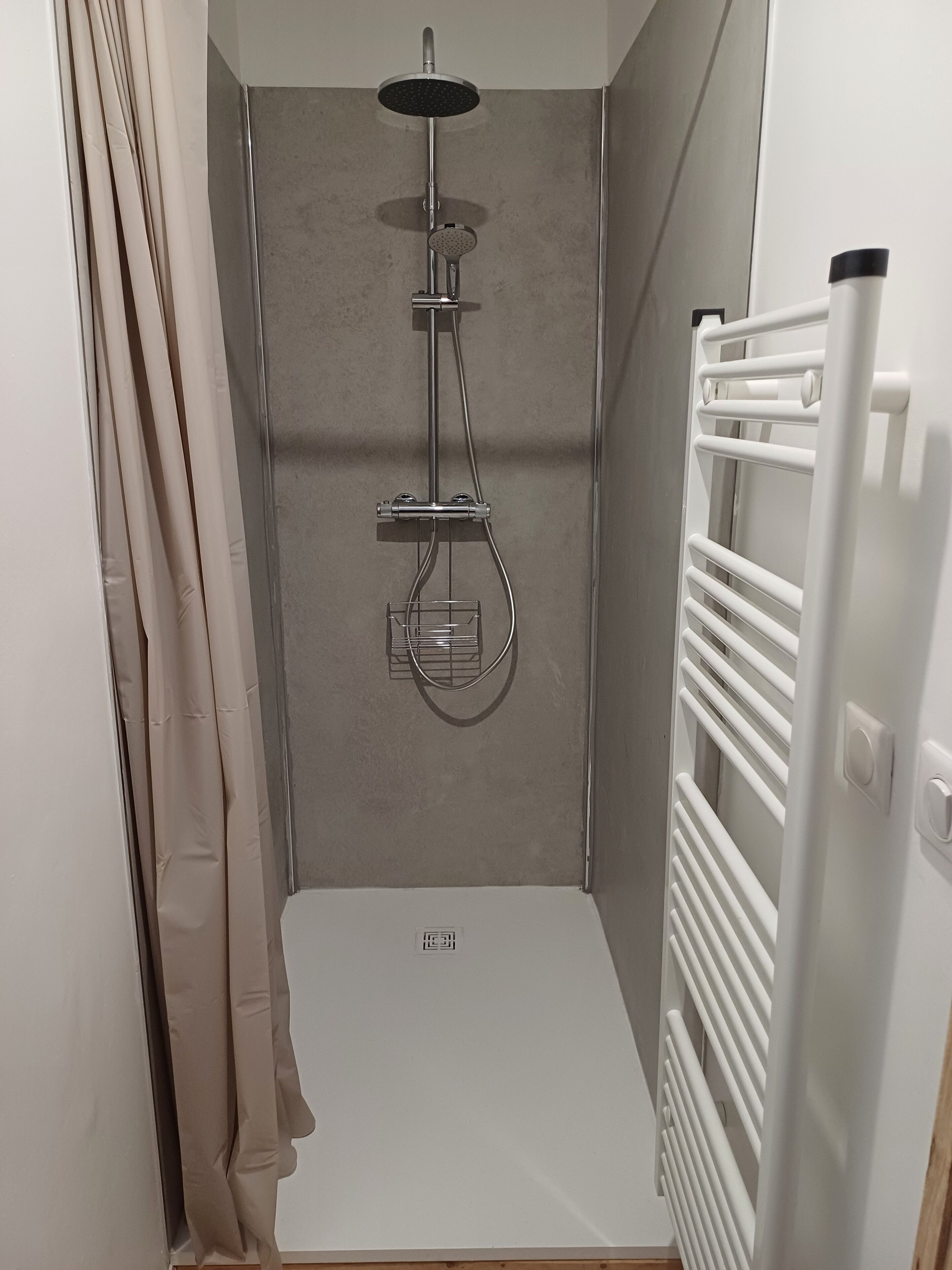 A shower with a handheld showerhead, a wall-mounted faucet, and a shower control panel.