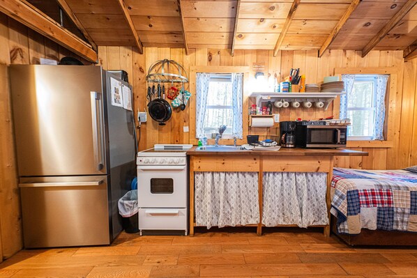 A compact kitchen with a stainless steel refrigerator, white stove, and a microwave. - Lakeside Cabin on Beach Pond with Sauna and Beach Access (Voluntown)