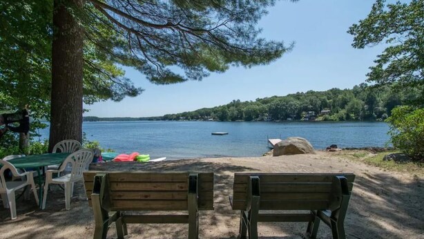 A lakeside view with a wooden bench, picnic table, and chairs.